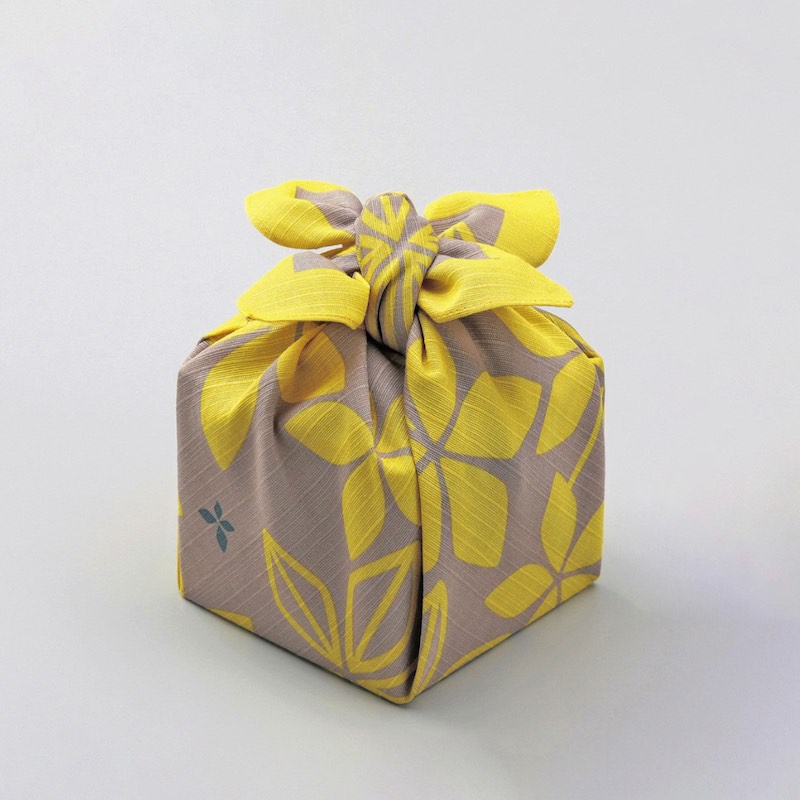 Furoshiki deocrated with yellow flowers wrapped around box.