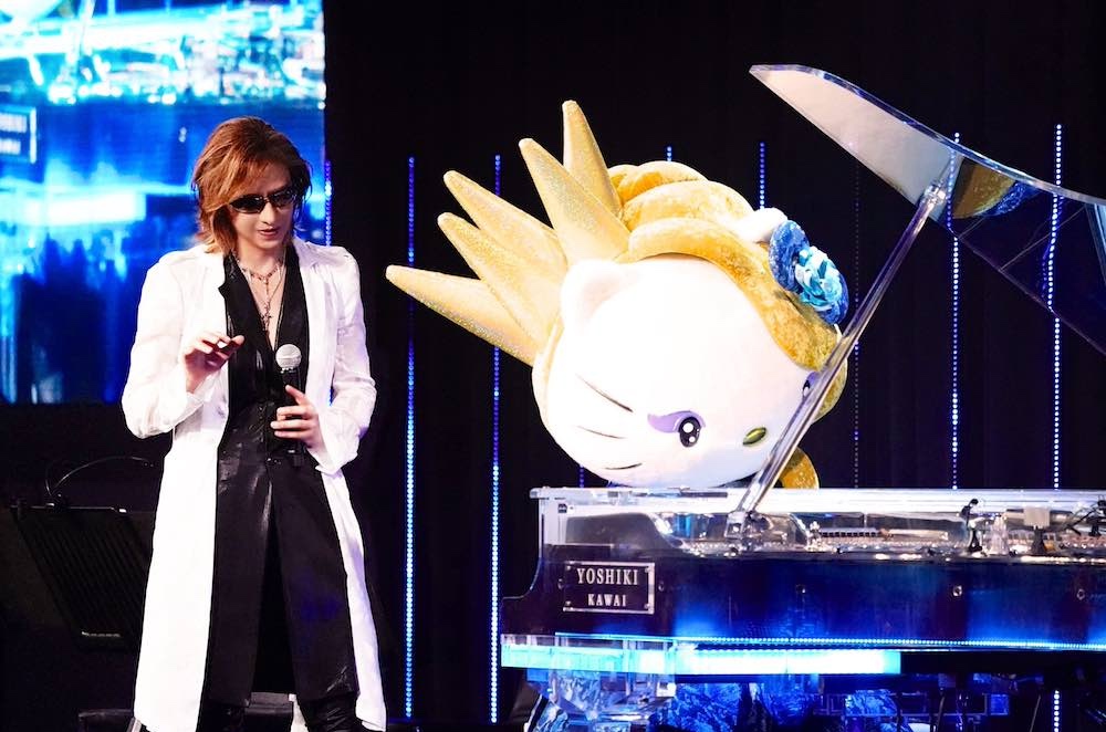 Japanese rock star YOSHIKI standing next to Sanrio character Yoshikitty who is playing a crystal piano