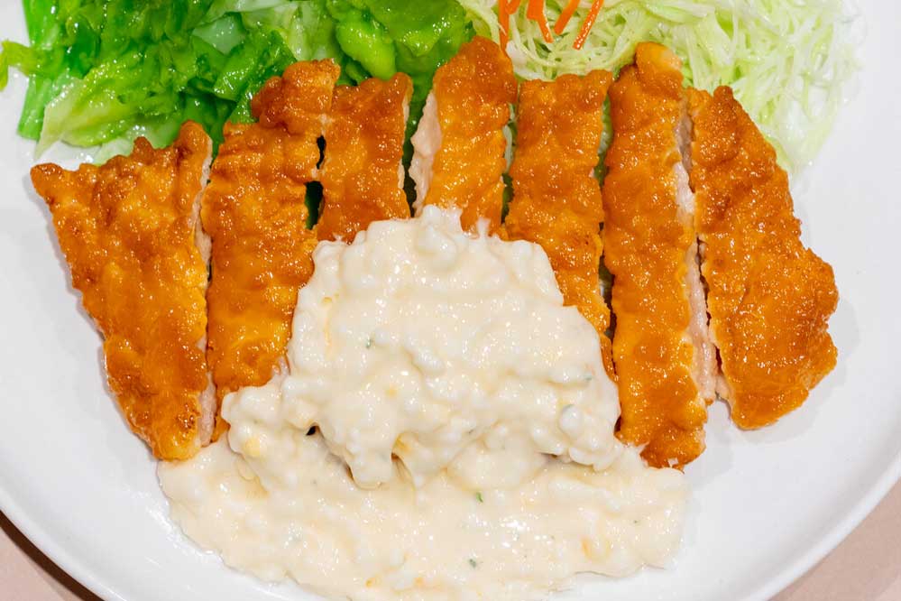 Food replica of chicken nanban and some greens on a white plate