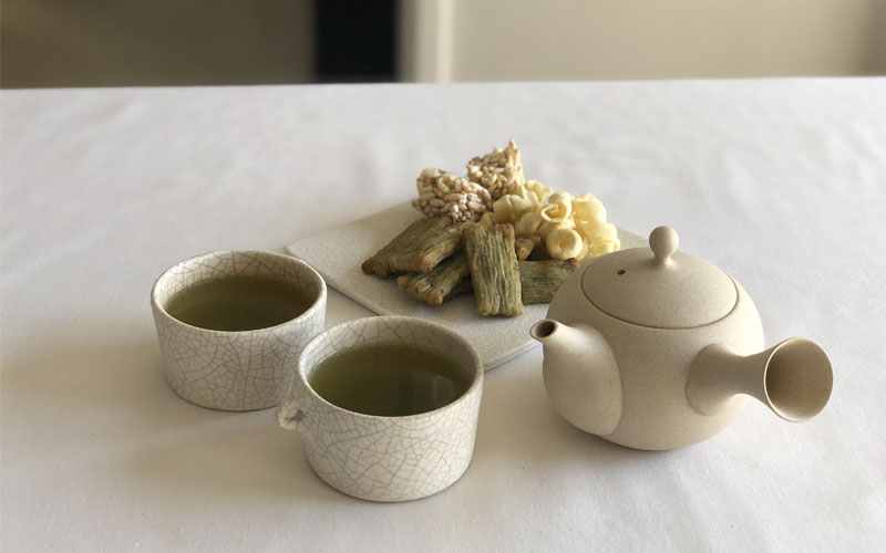 A teapot, two cups of tea, and Japanese snacks on a plate