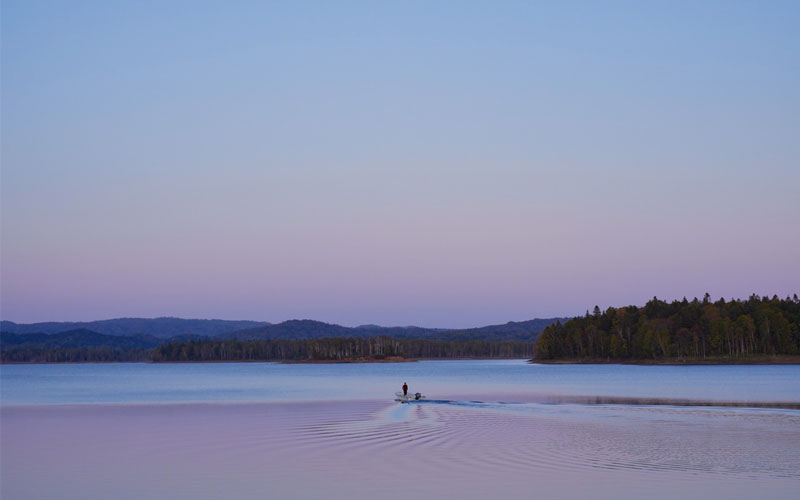 A boat floats peacefully on calm waters in Hokkaido, with distant mountains in view.