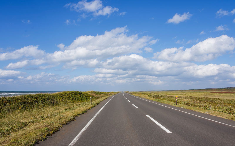 Scenic Hokkaido road cutting through a wide open landscape beneath a bright blue sky.