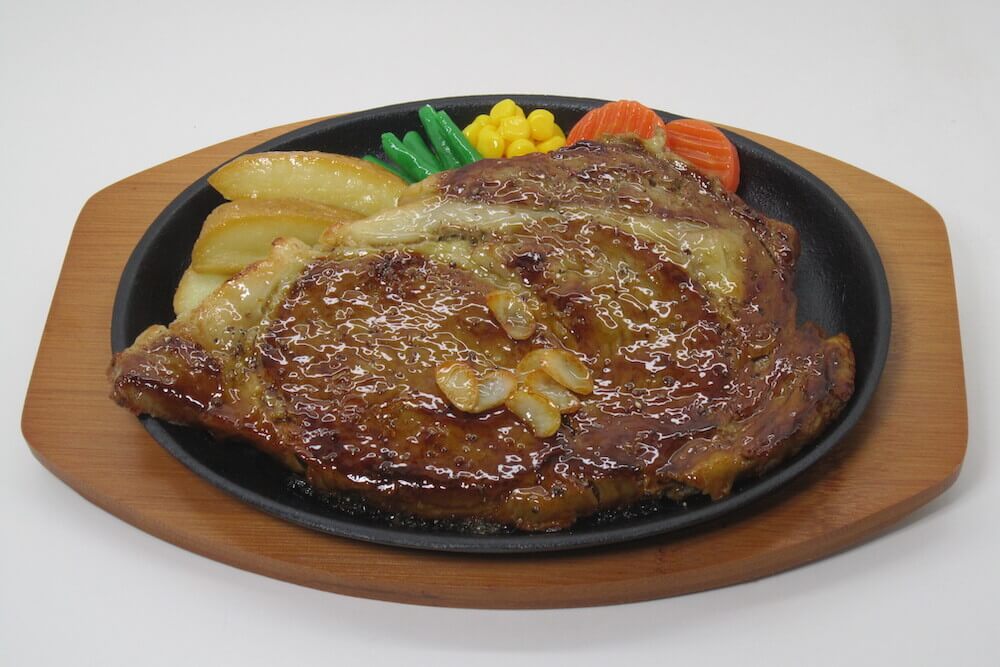 Plastic model of a grilled steak with vegetables, used in restaurant displays.