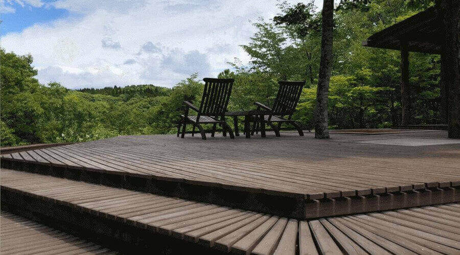 A wooden deck with chairs overlooking a lush green forest, likely in the Kirishima Mountain Range, Japan. 