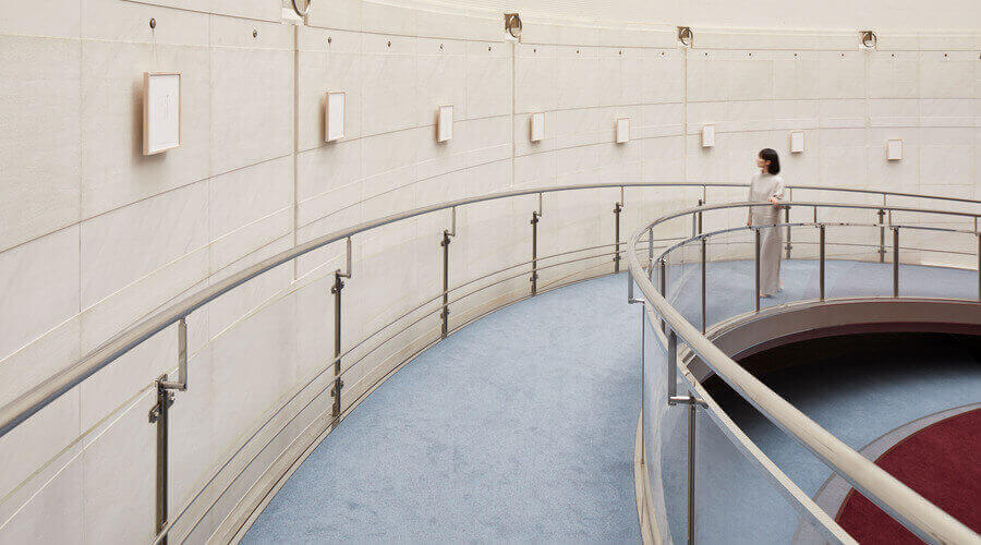 Woman views minimalist art in a curved, modern gallery with a sleek railing and light carpet.