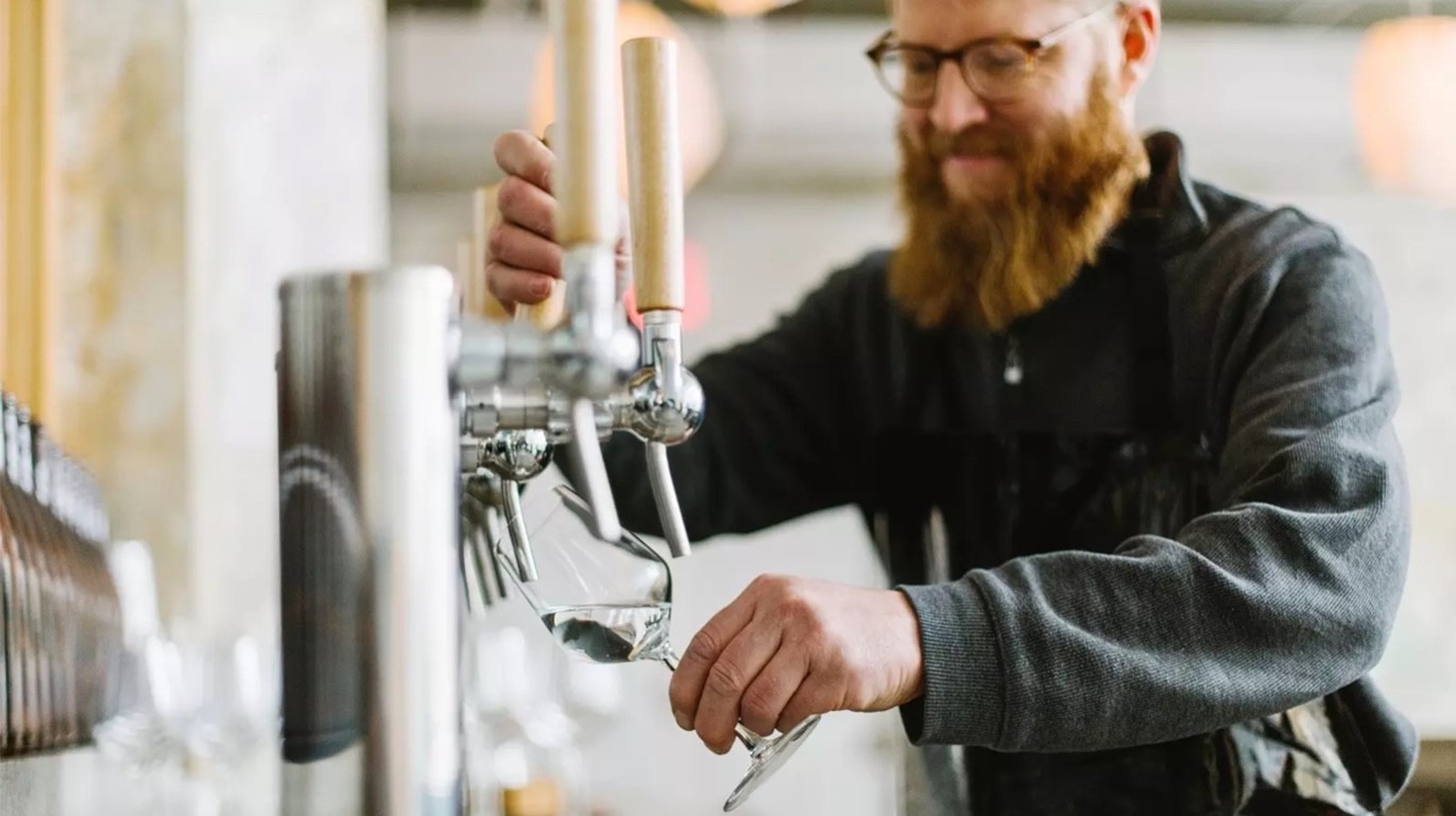 Man with beard pouring sake from tap at Brooklyn Kura brewery.